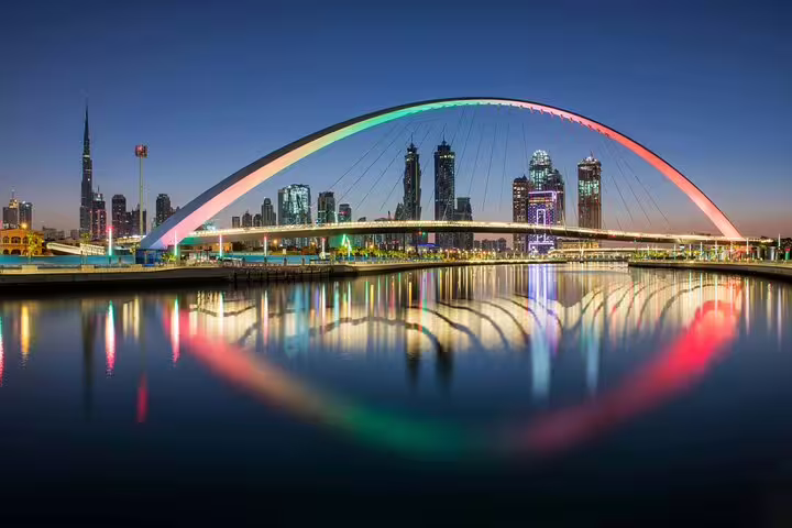 Dubai skyline at night with a vibrant, illuminated bridge reflecting on the water, part of a modern city tour.