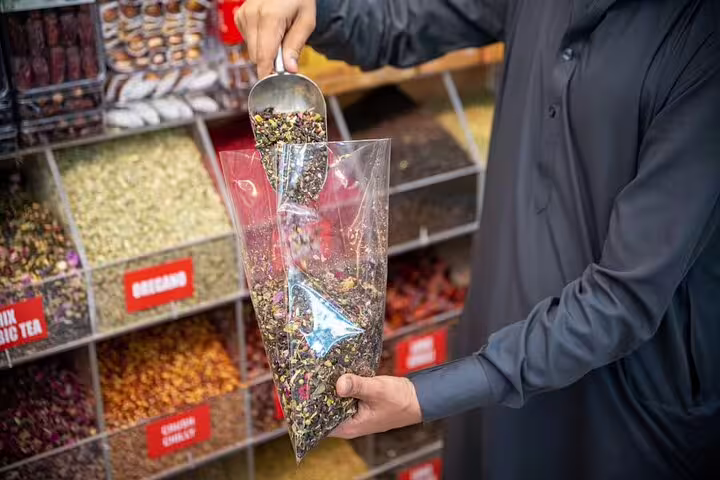 Guide scooping colorful loose tea and spices into a bag at a bustling Dubai spice souk on a guided walking tour