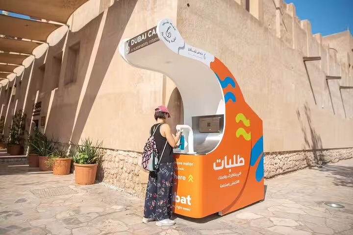 Traveler refilling bottle at modern Dubai water station during guided walking tour near historic Al Fahidi neighborhood