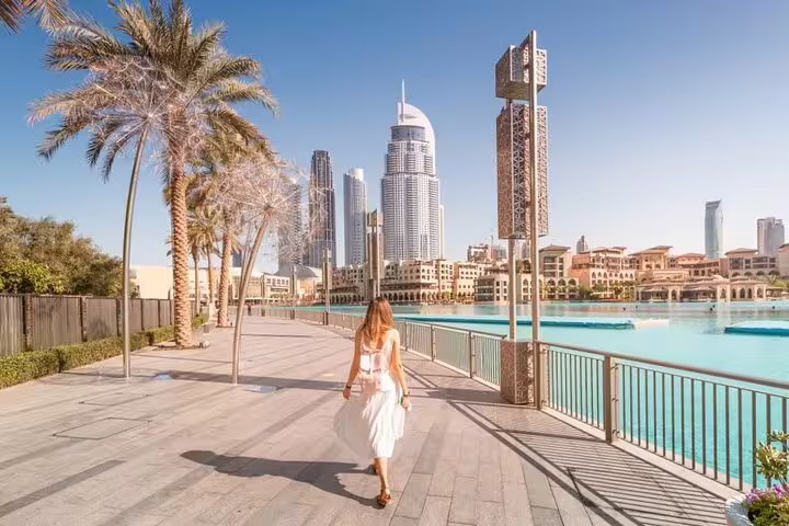 Woman strolling along Dubai waterfront promenade with skyline view on a sunny day during city sightseeing tour.