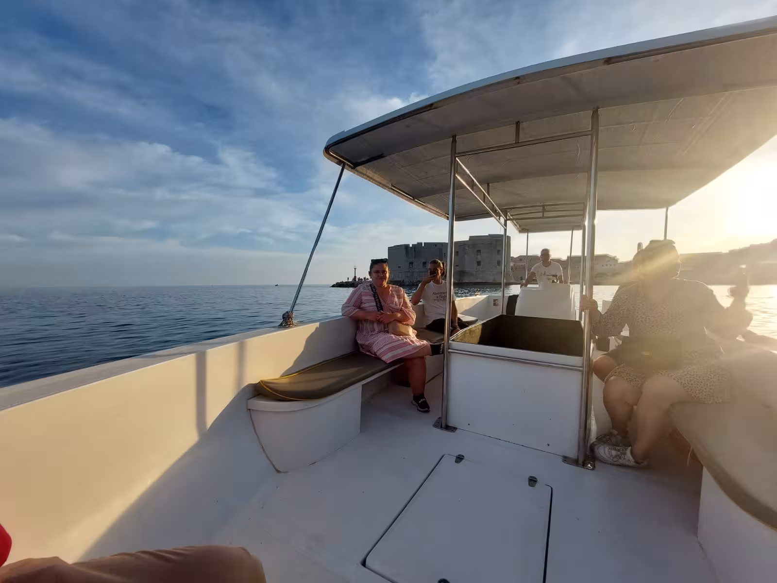 Guests relaxing on a boat at sunset with Dubrovnik Old Town walls in view, panorama cruise after history walk