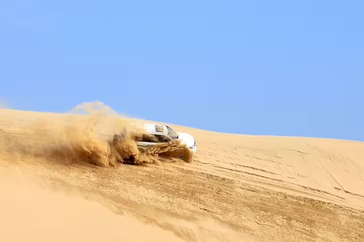 Thrilling dune bashing adventure with a 4x4 vehicle kicking up sand under a clear blue sky.
