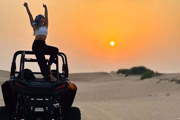 Traveler standing on dune buggy with arms raised at sunset, enjoying desert quad bike ride and dune bashing