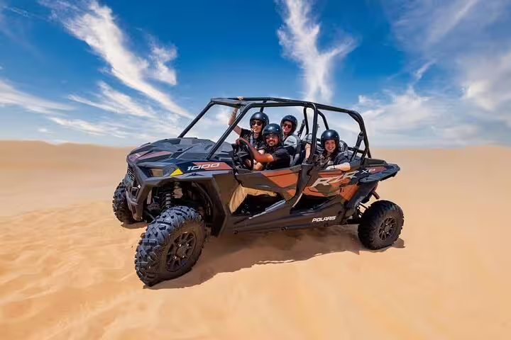 Group enjoying a thrilling dune buggy ride in Dubai's desert, under a clear blue sky with vast sandy vistas.