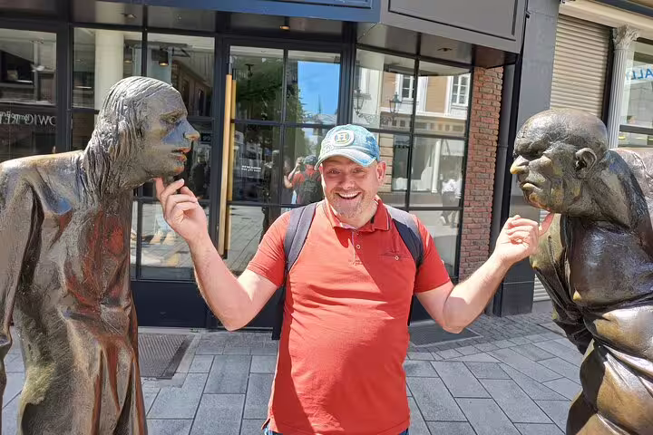Smiling traveler between Düsseldorf Altstadt bronze figures during a self-guided scavenger hunt tour