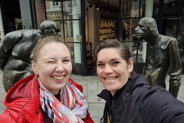 Friends pose by Düsseldorf bronze street sculptures, fun stop on a self-guided scavenger hunt tour