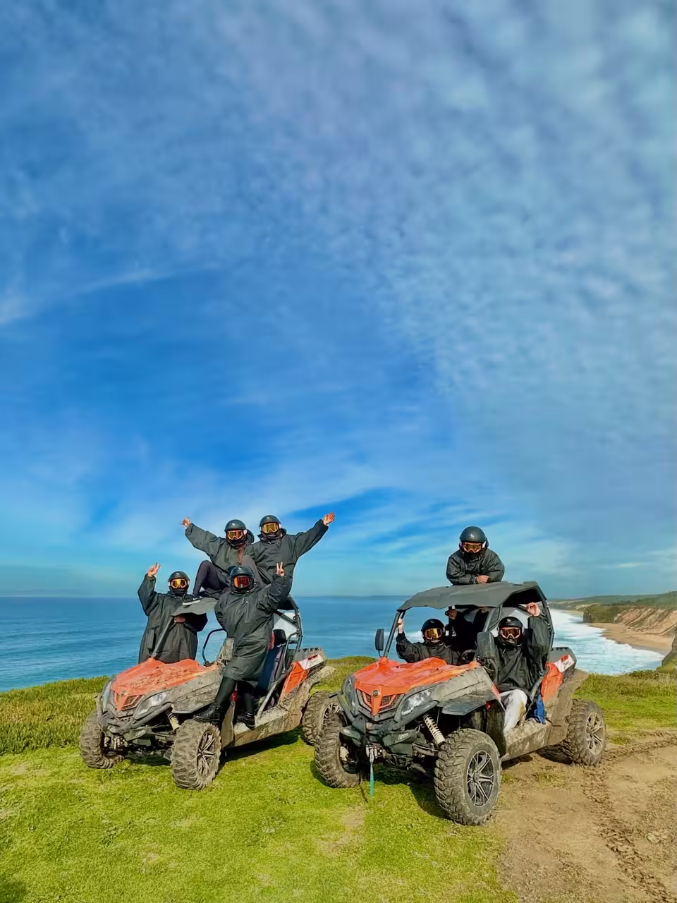 Group in helmets posing on dune buggies above the ocean during Dust Breaker Buggy Tour, scenic coastal cliffs