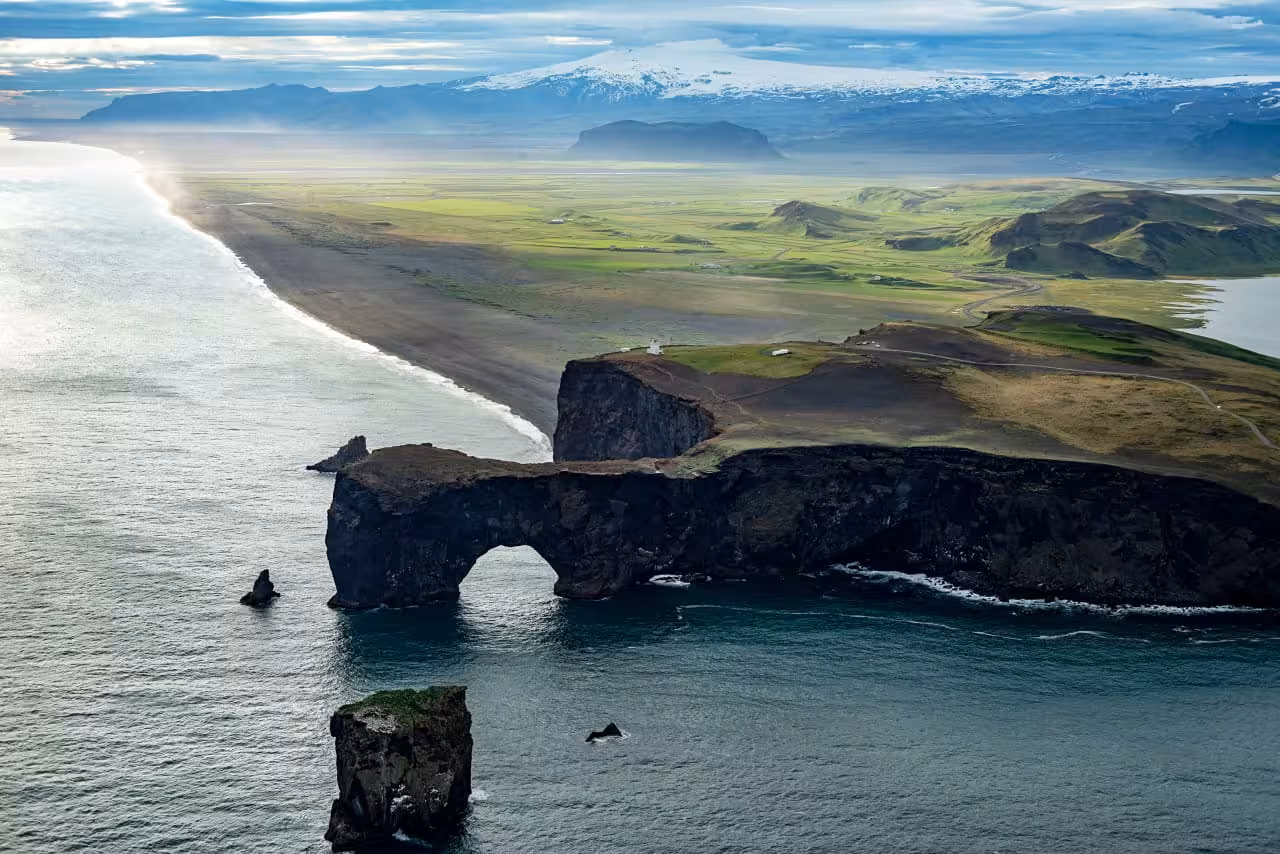 Aerial view of Dyrhólaey Arch on Iceland's South Coast, surrounded by ocean and lush green landscape.
