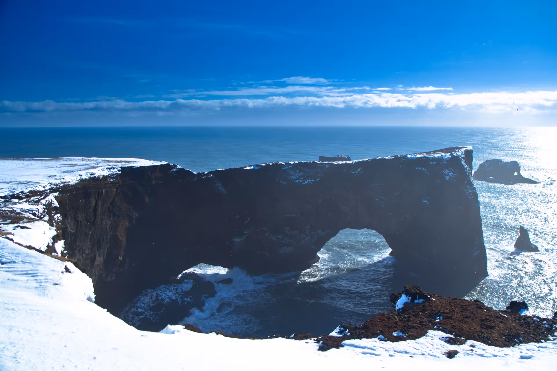 Snow-covered Dyrhólaey arch against the ocean backdrop on Iceland's south coast.