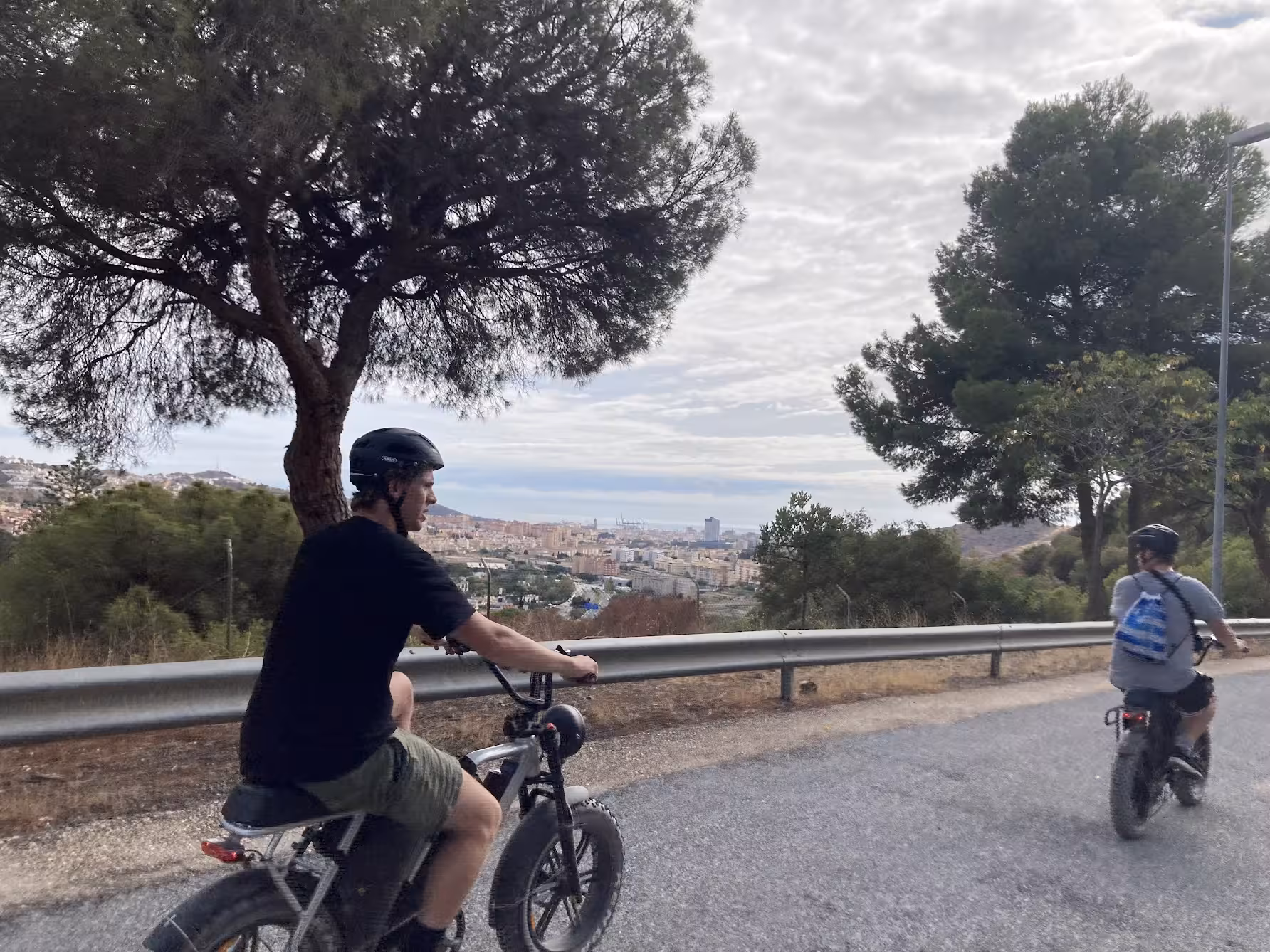 Riders on e-fat bikes cruising a hillside road with panoramic coastal city views on a 4-hour rental