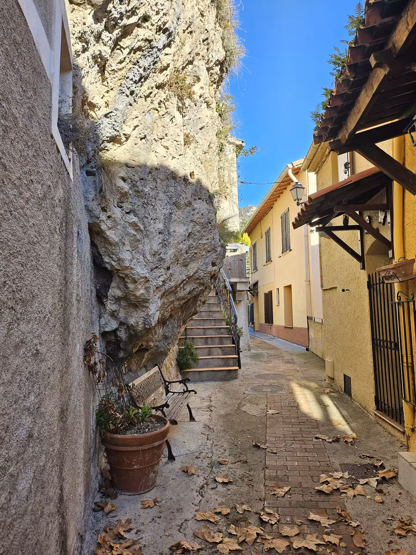 Charming narrow alley in East Côte d'Azur with rocky cliffs and rustic buildings bathed in sunlight.