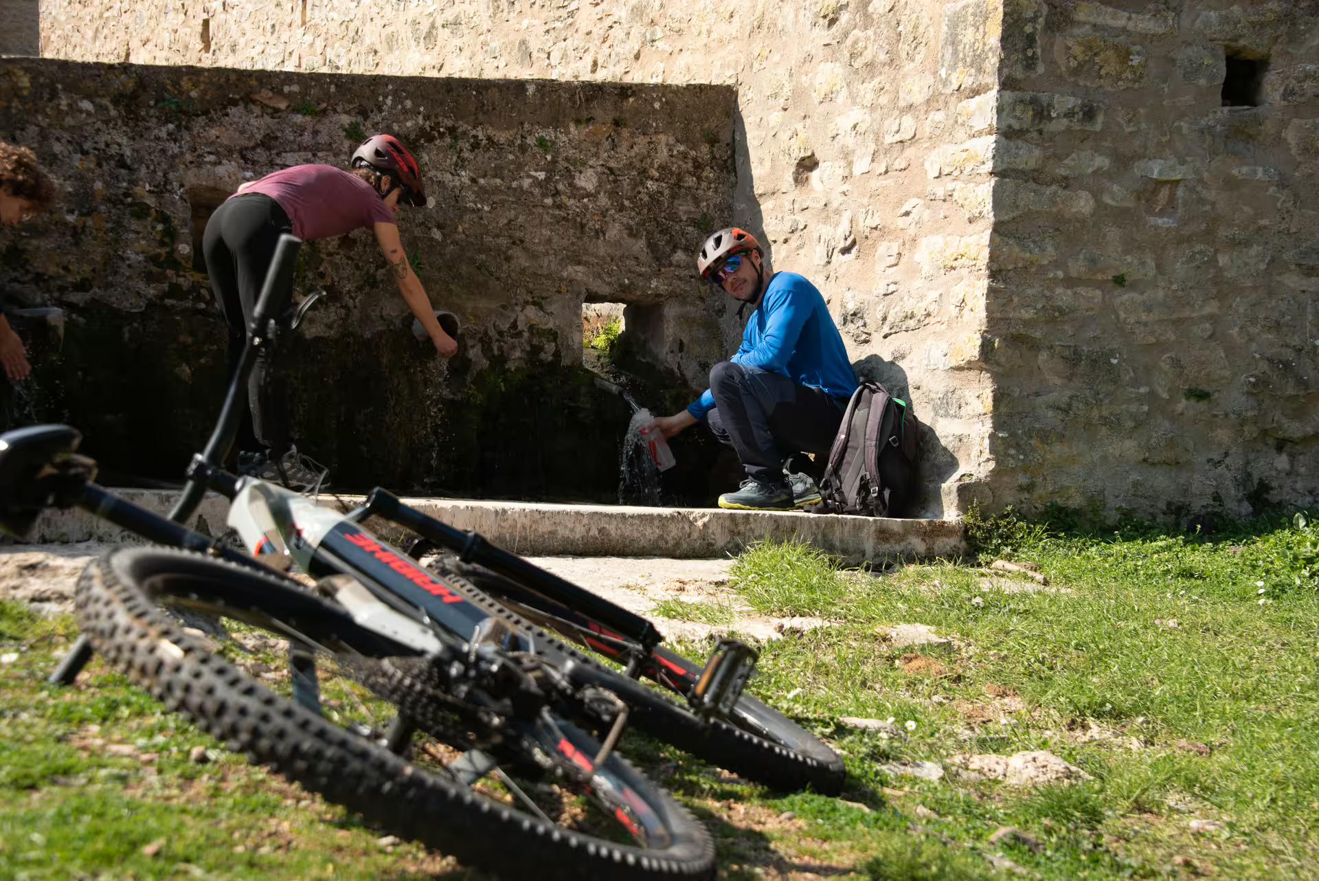 E-bike riders refill water at a stone spring stop on the Ancient Messene Way guided e-bike tour in Greece