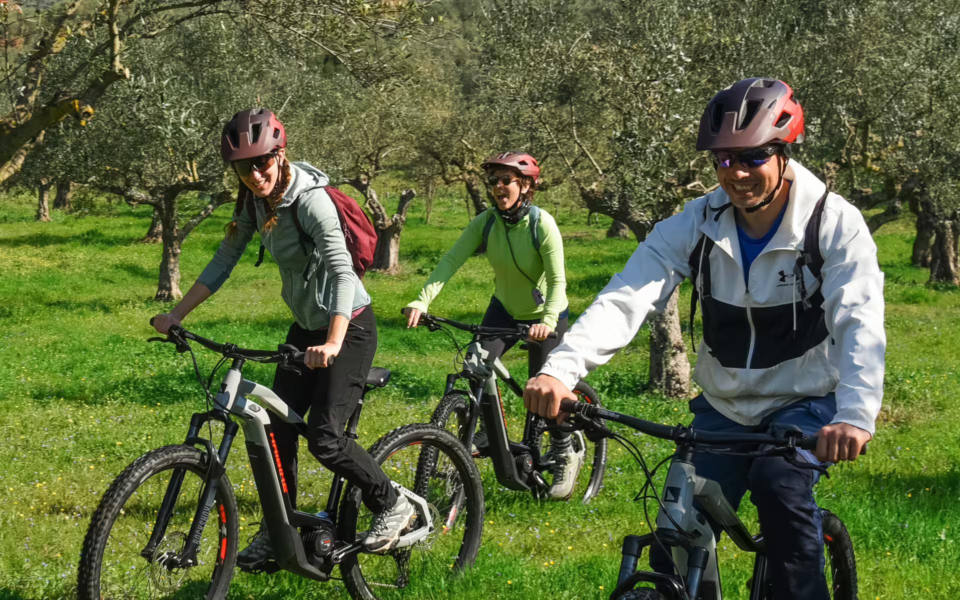 Smiling group on e-bikes riding through olive groves in Messinia, Greece on the Ancient Messene Way tour