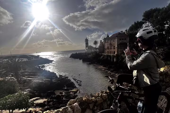 Cyclist captures scenic sunset over Cascais coastline with lighthouse backdrop on e-bike tour.
