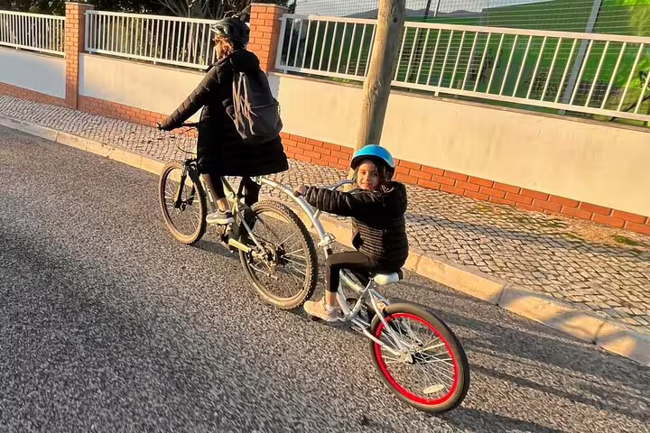 Parent and child enjoying an e-bike ride through a sunny street in Cascais on a family-friendly tour from Lisbon.