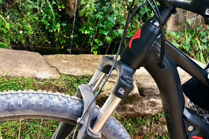 Close-up of an e-bike front wheel and suspension against a rustic stone wall in Cascais and Sintra backroads.