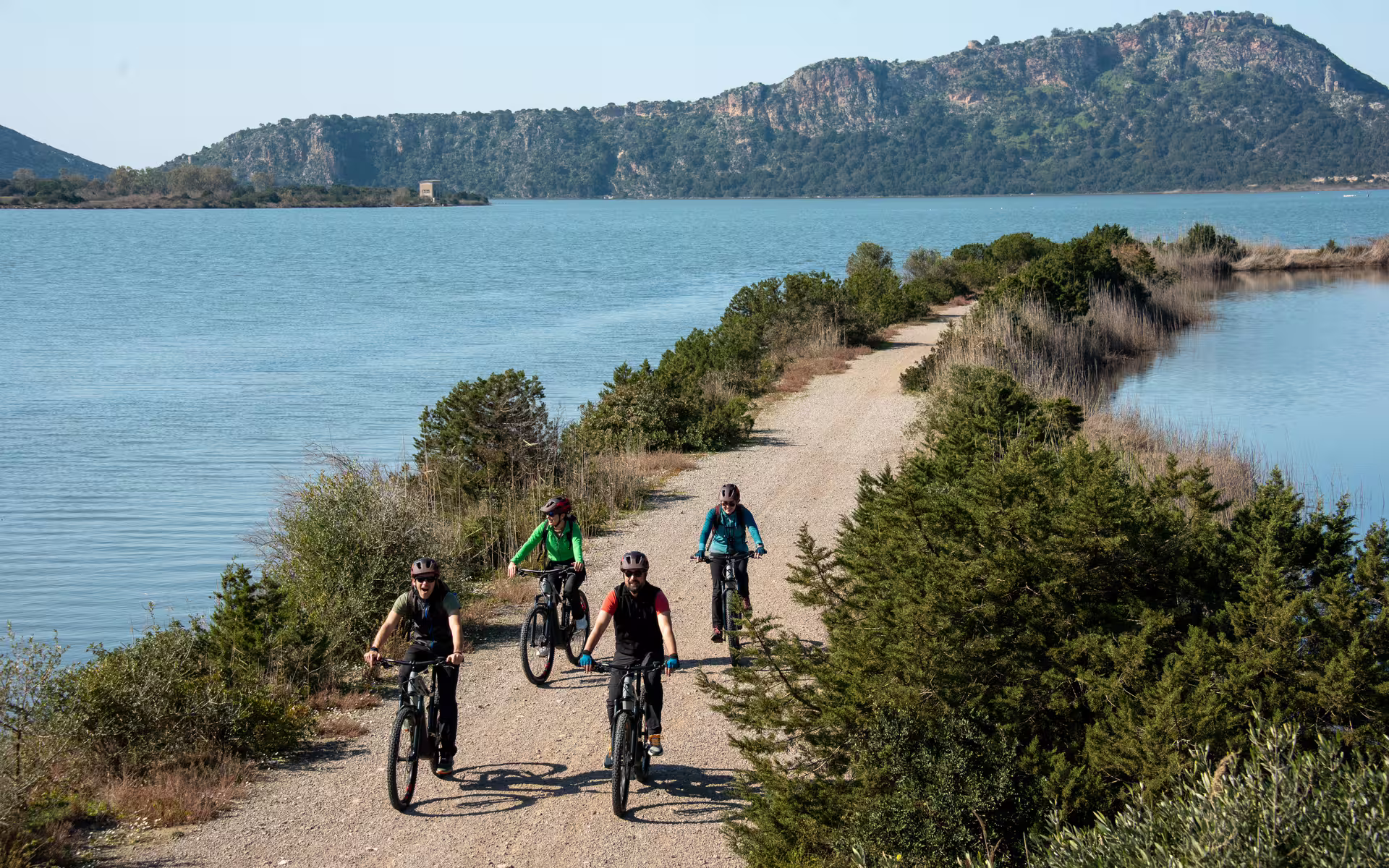 Group riding e-bikes on Navarino Trail beside Gialova Lagoon, Messinia, with sea views and hills