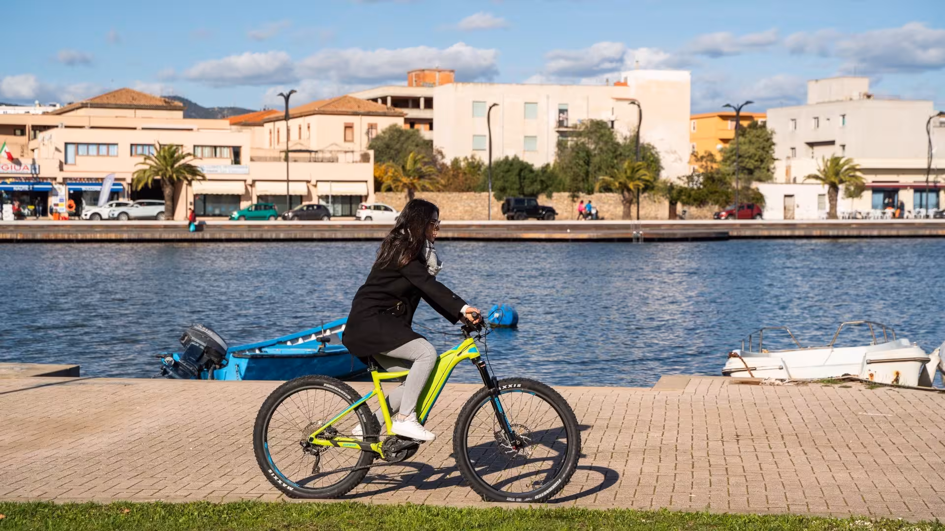 Close-up of a person enjoying an e-bike ride by the marina in Sardinia, showcasing the vibrant waterfront of Olbia.