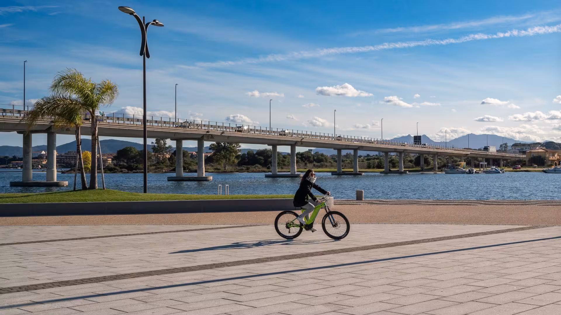 E-bike rider exploring the beautiful waterfront and bridge views in Olbia, Sardinia, perfect for a serene holiday adventure.