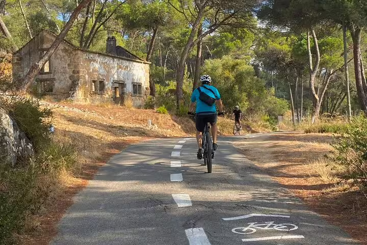 Cyclists enjoy a scenic e-bike ride through lush forest trails in Cascais and Sintra, passing an old stone building.