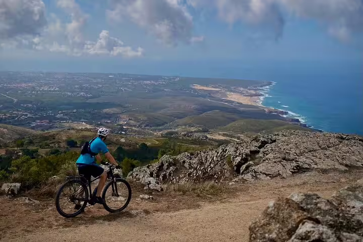 E-bike rider on a cliffside trail overlooking the expansive coast from Sintra Mountains to Cascais Sea.