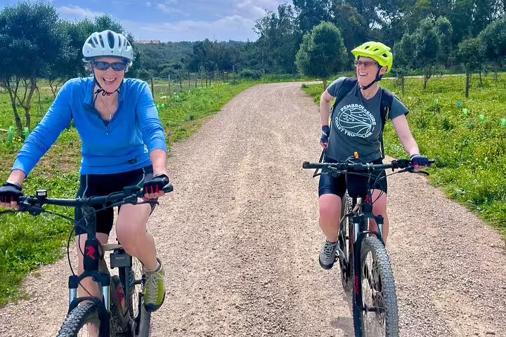 Two cyclists smiling as they ride e-bikes through lush trails in the Sintra Mountains en route to Cascais.
