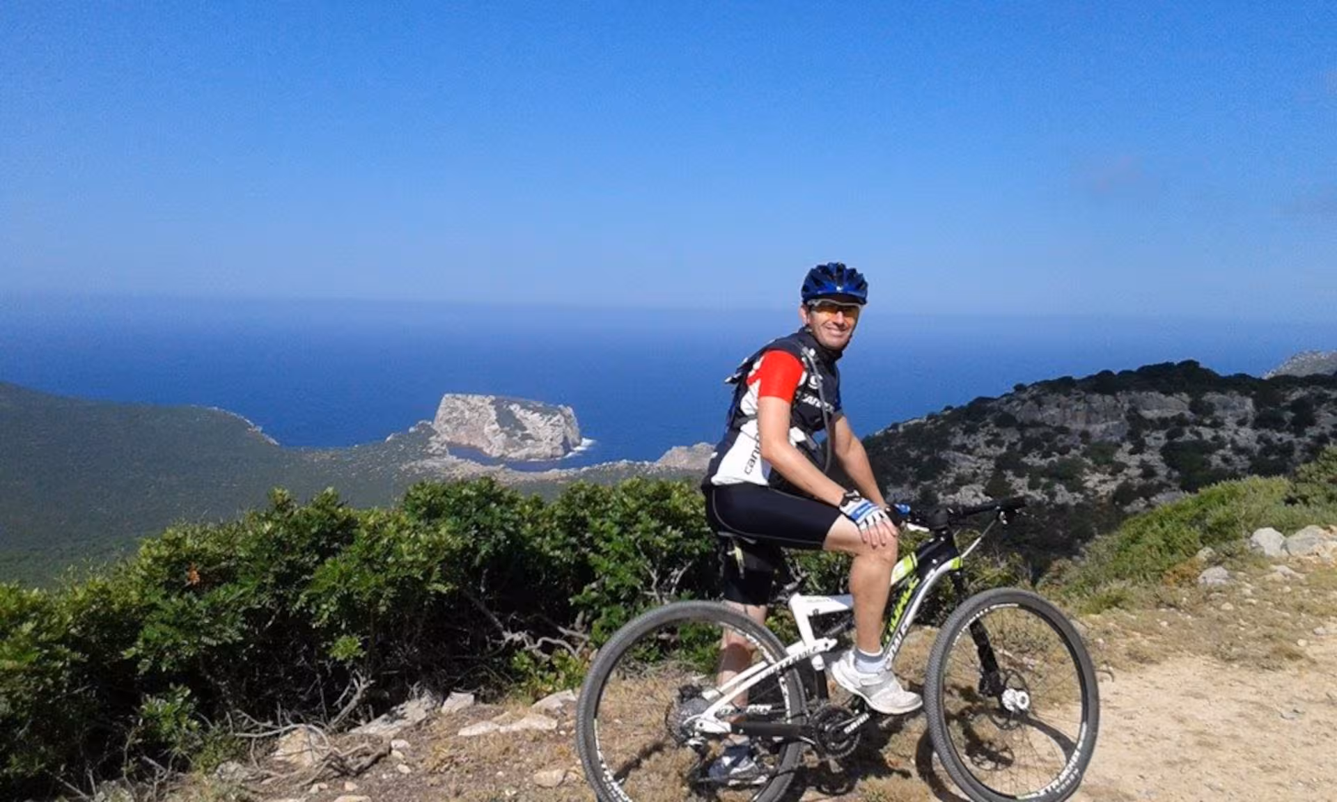 Cyclist pauses on an e-bike tour to admire the breathtaking view of Alghero's rugged coastline and azure sea.