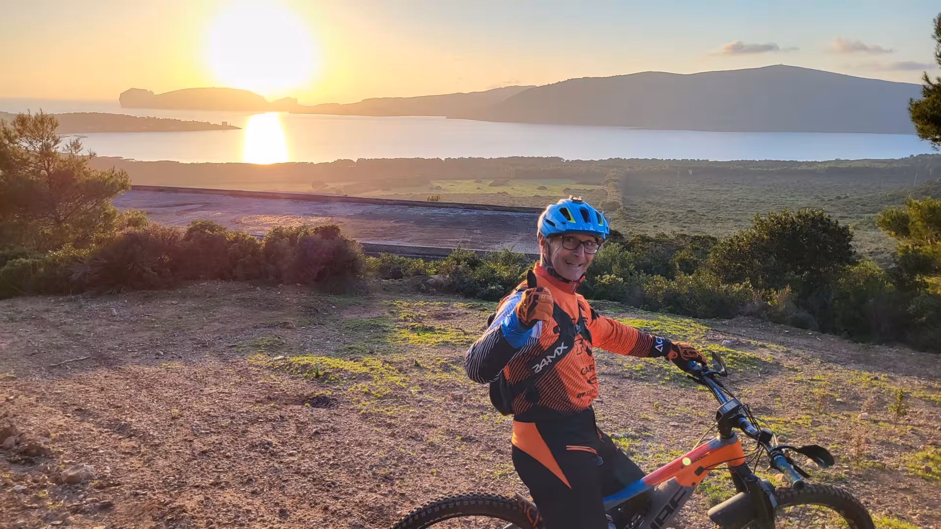 Cyclist on an e-bike at sunset overlooking Alghero coastline, capturing a serene and picturesque landscape.