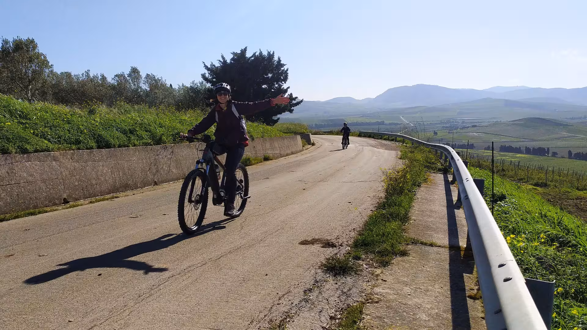 A biker extends arms joyfully while riding along a scenic vineyard path in Castellammare del Golfo.