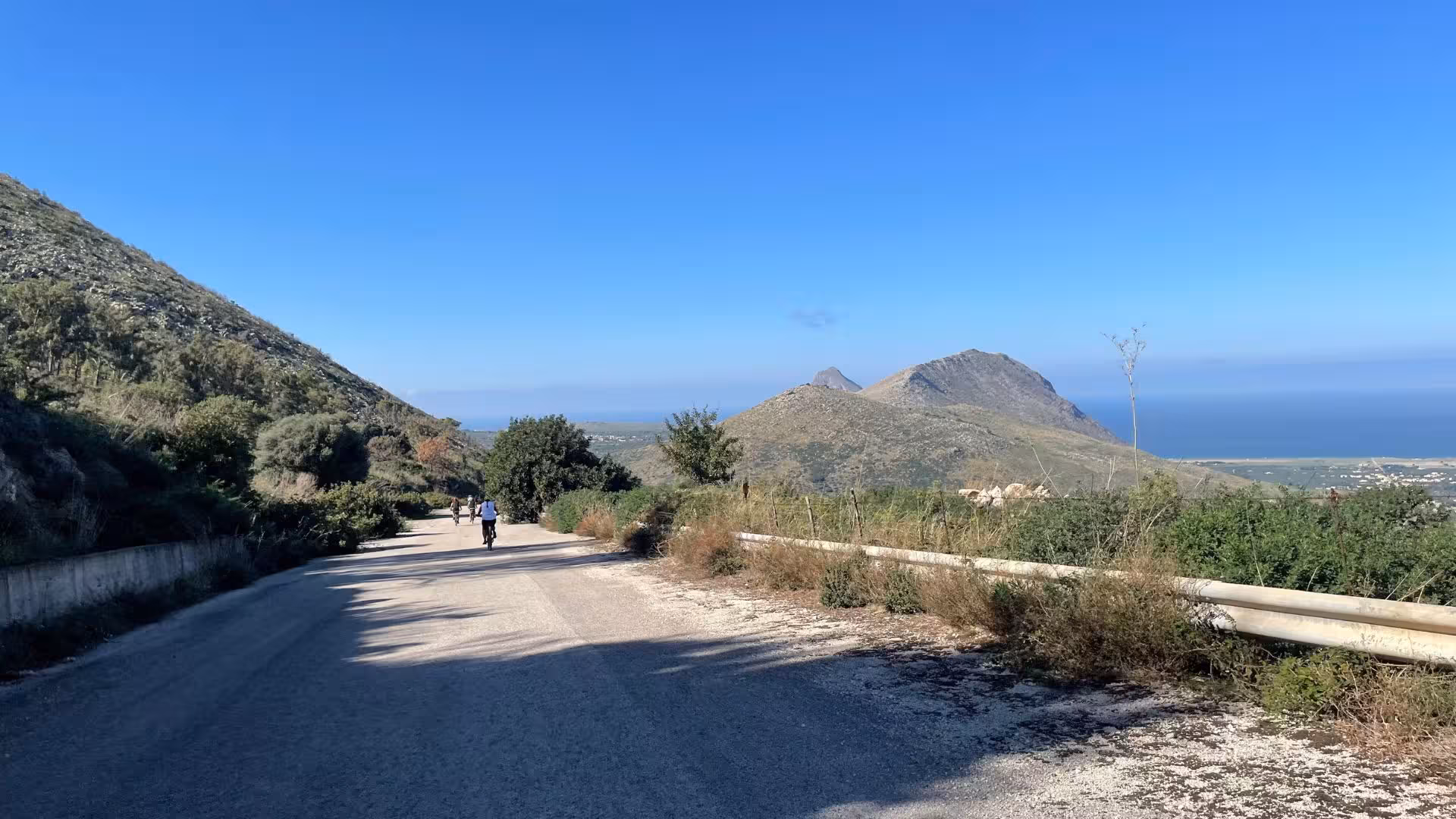 Cyclists enjoying scenic ebike tour on winding road with lush hills and coastal views in Erice.