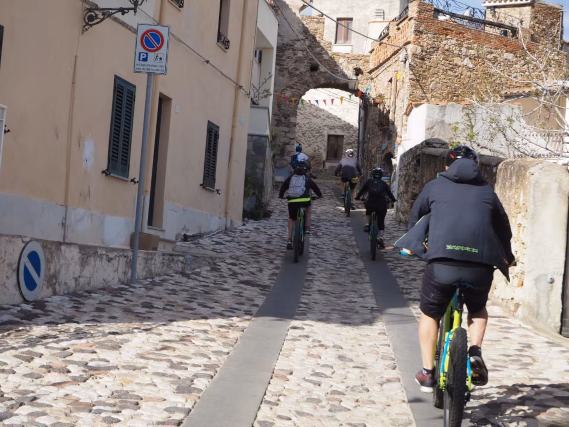 E-bike tour group navigating through a charming cobblestone street in a Sardinian village.