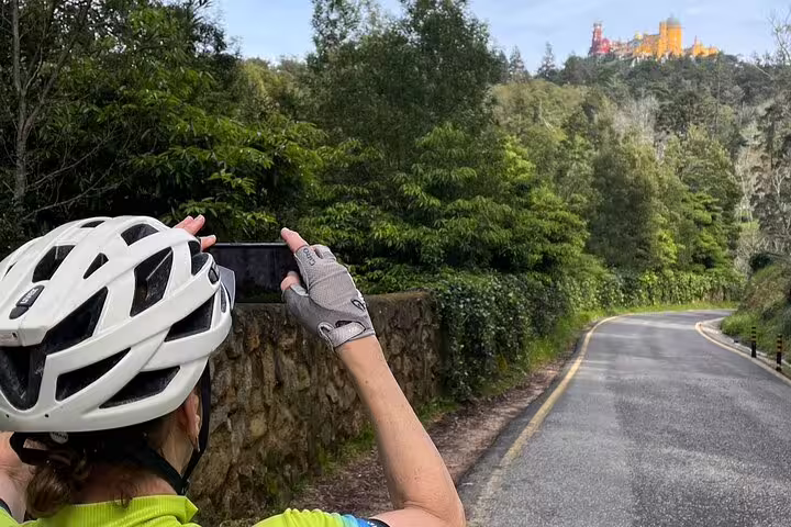 Cyclist taking a photo of Pena Palace in Sintra Mountains during an e-bike tour from Lisbon to Cascais.