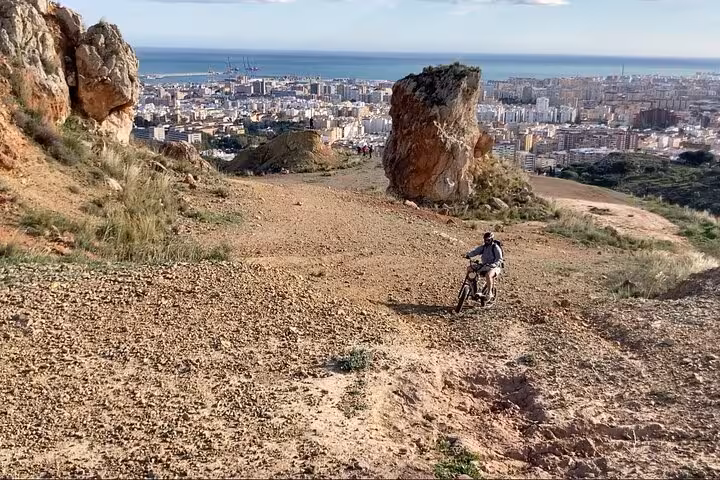 Solo rider descending a rocky off-road trail in the Montes de Malaga with Malaga city and sea views below