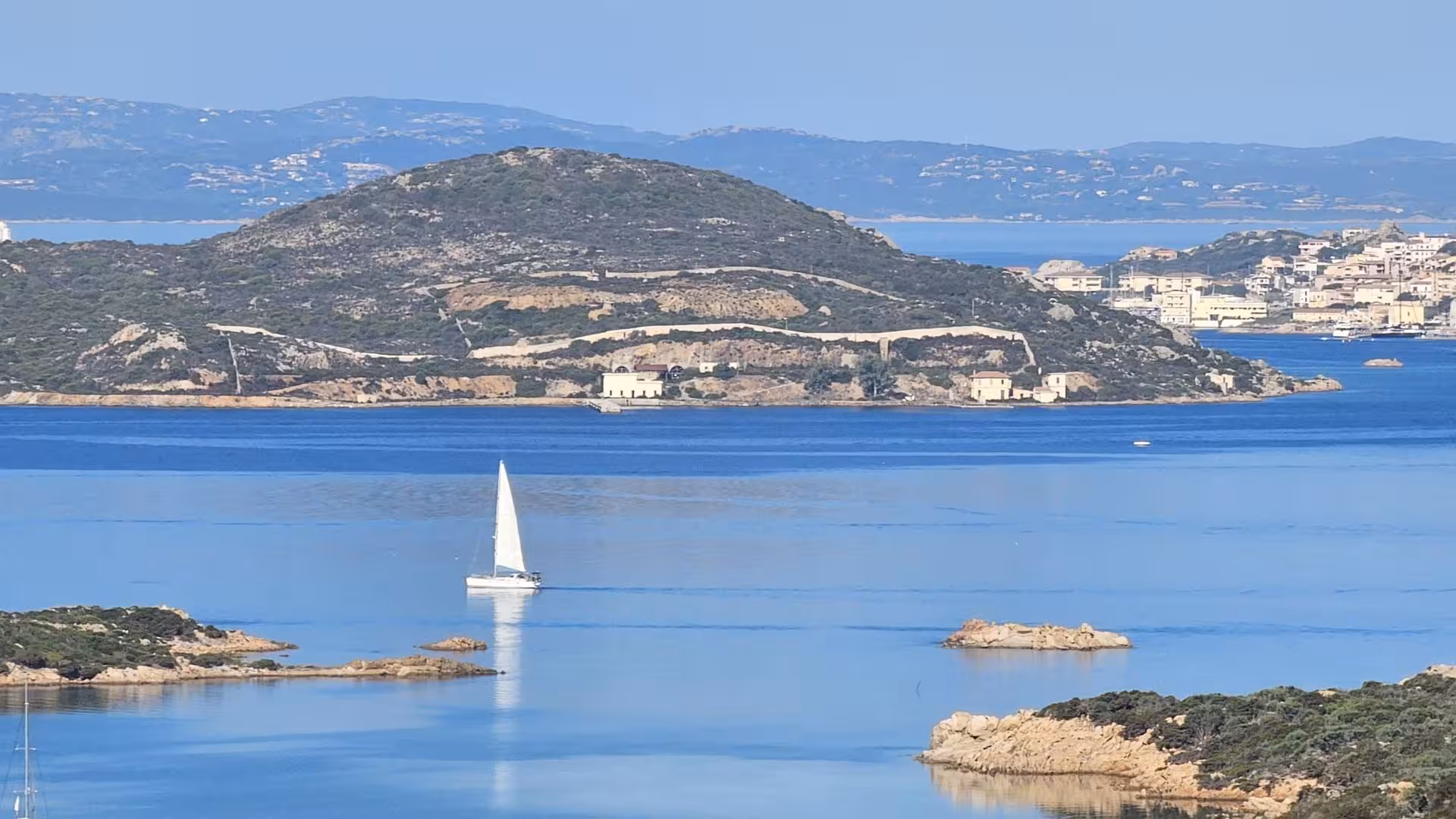 Sailboat gliding across blue waters with scenic views of Caprera Island during an e-bike tour from Palau.
