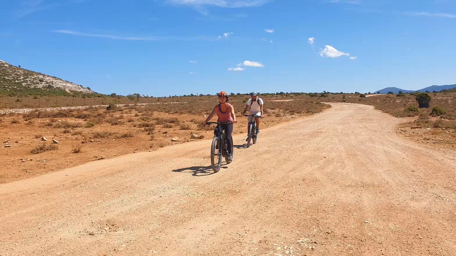 Cyclists enjoy an ebike tour on a scenic dirt path in the rugged Supramonte landscape under a clear blue sky.