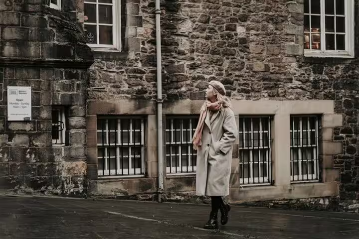 Woman walking by rustic stone building, capturing timeless Edinburgh charm for a unique photoshoot.