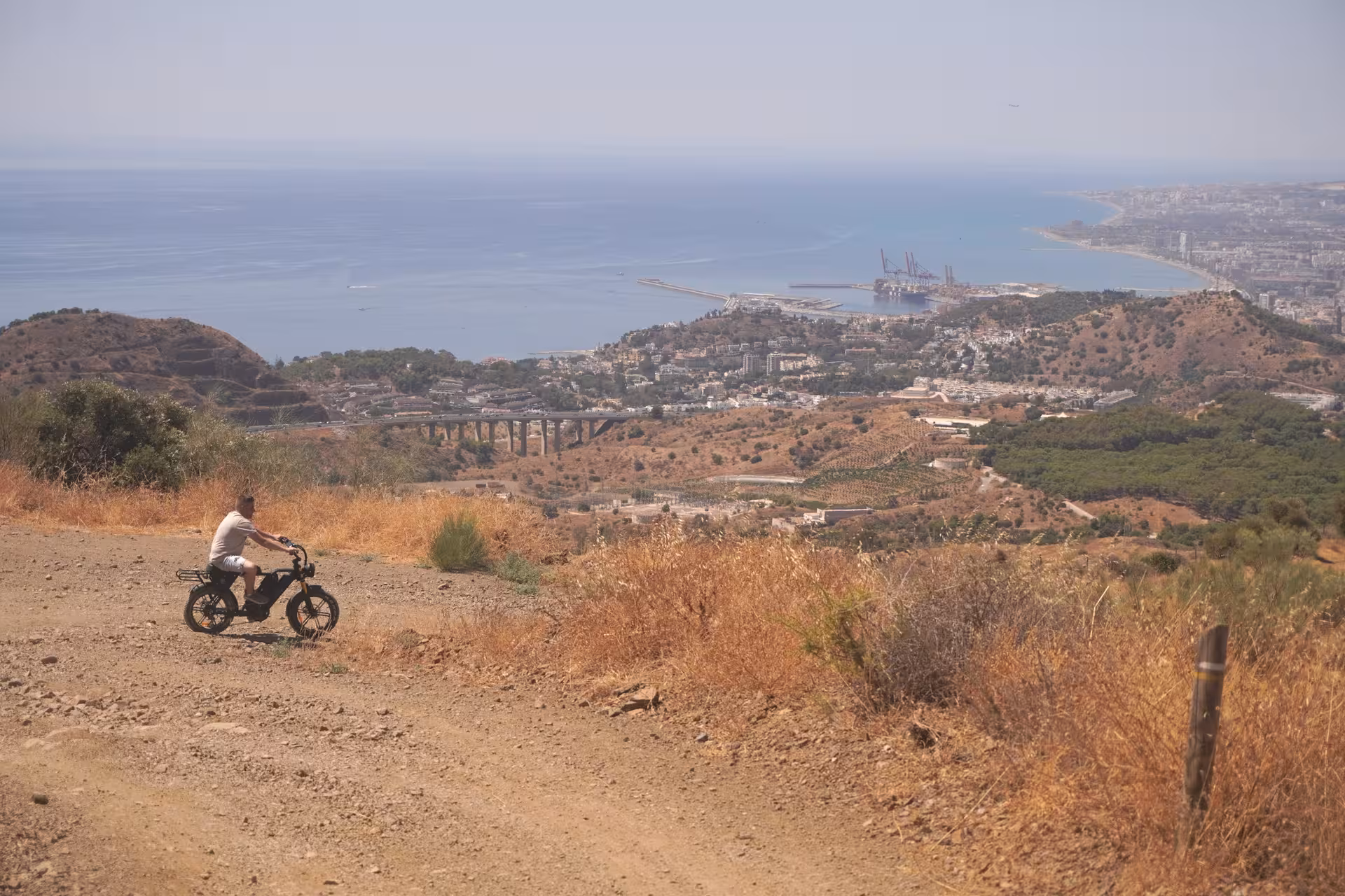 E-fat bike rider on a mountain trail with sweeping coastal views and seaside city skyline on a 4-hour rental
