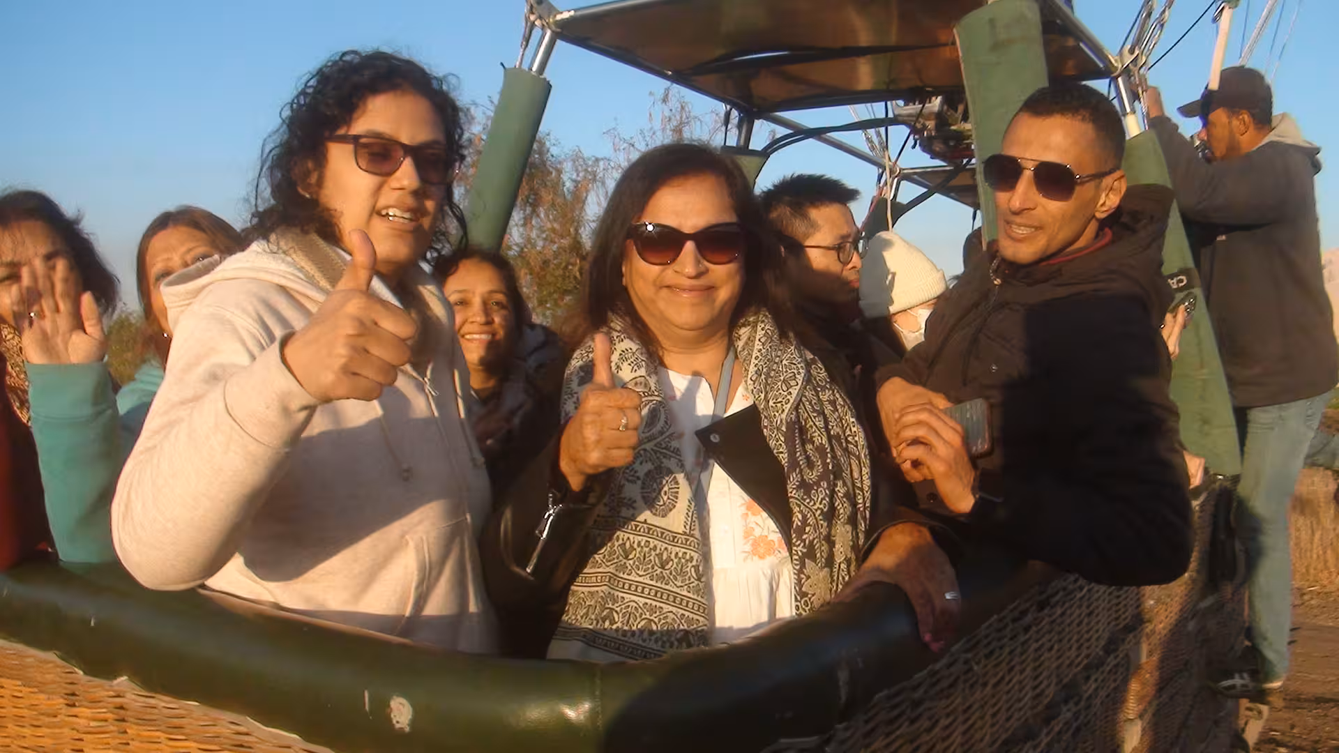 Group of travelers giving thumbs up in a hot air balloon basket, enjoying a sunrise adventure in Egypt.