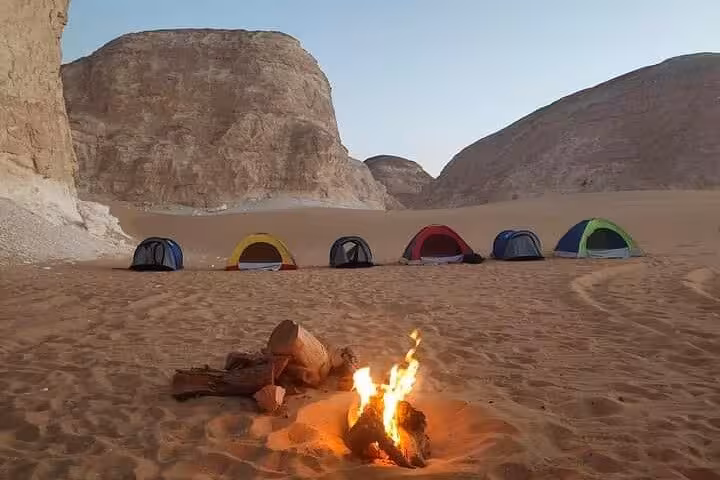 Cozy campfire and colorful tents in the stunning backdrop of Egypt's White Desert during an all-inclusive overnight tour.