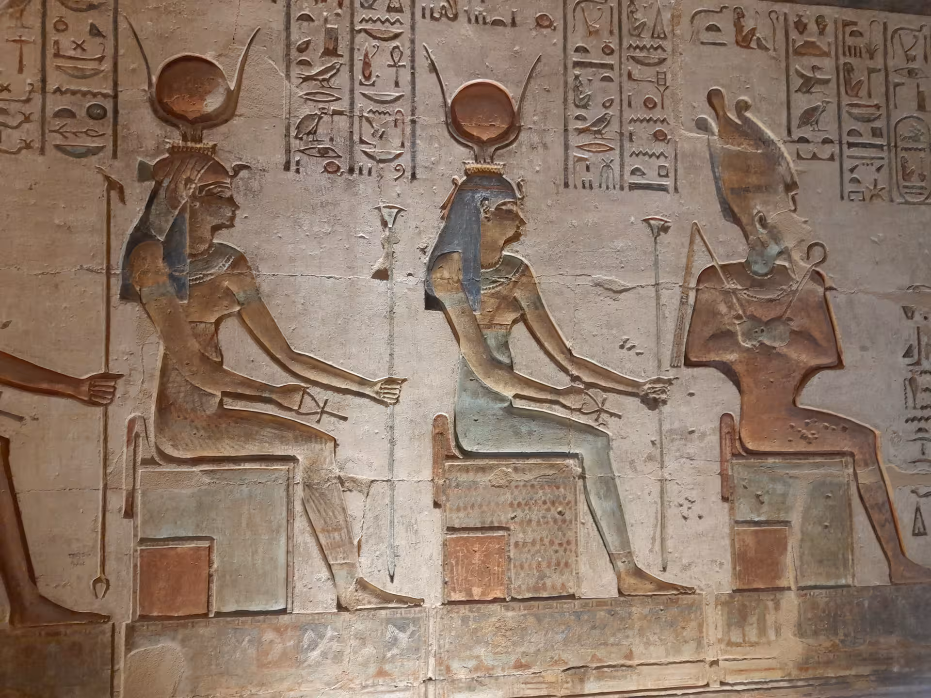 Colorful depictions of Egyptian deities on a temple wall, featuring hieroglyphics and ancient religious symbolism.