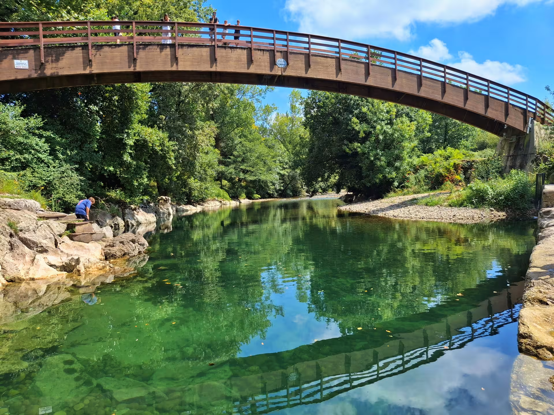 Scenic view of a bridge over a tranquil river surrounded by lush greenery near El Castillo Caves.