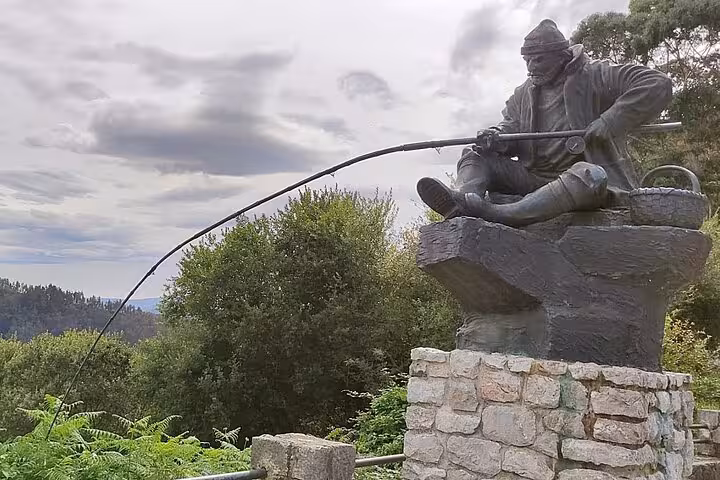Statue of a fisherman with a rod, surrounded by greenery, near El Soplao Cave tour from Torrelavega.