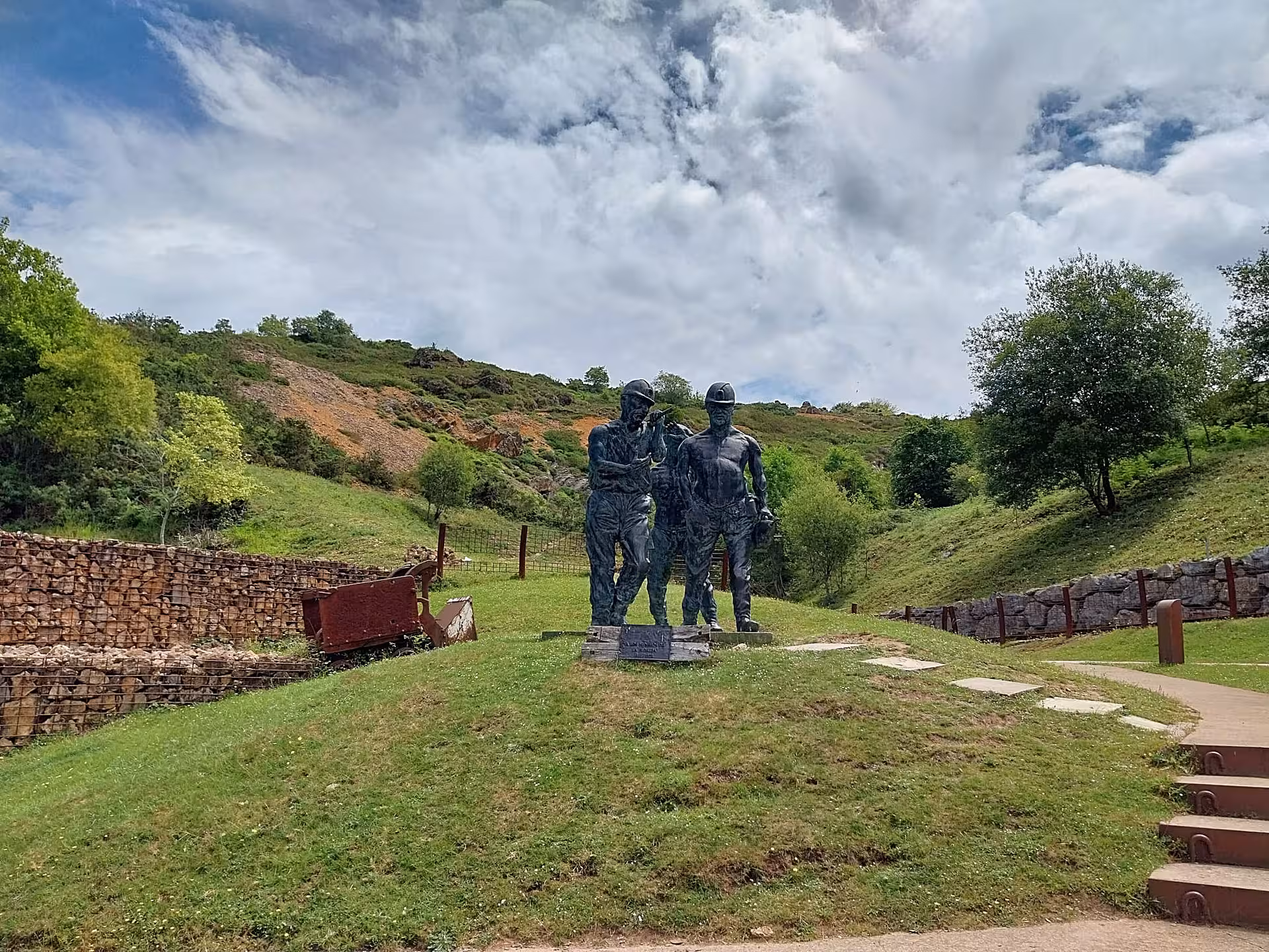 Statue of miners at El Soplao Cave entrance, surrounded by lush green hills, highlighting cultural heritage.