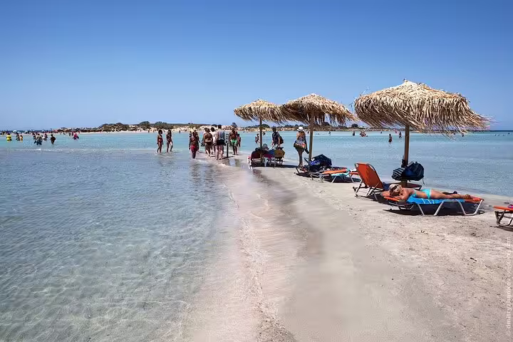 Tourists relax under straw umbrellas on the pink sands of Elafonisi Beach, Crete, during a private tour from Chania.