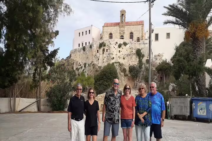 Group of tourists enjoying a private tour near a historic building on the way to Elafonisi Beach's pink sands from Chania.
