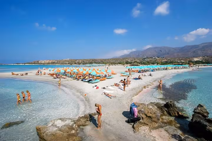 Elafonissi Beach sandbar with pink-tinged sand, swimmers and umbrellas, popular Rethimno to Crete tour