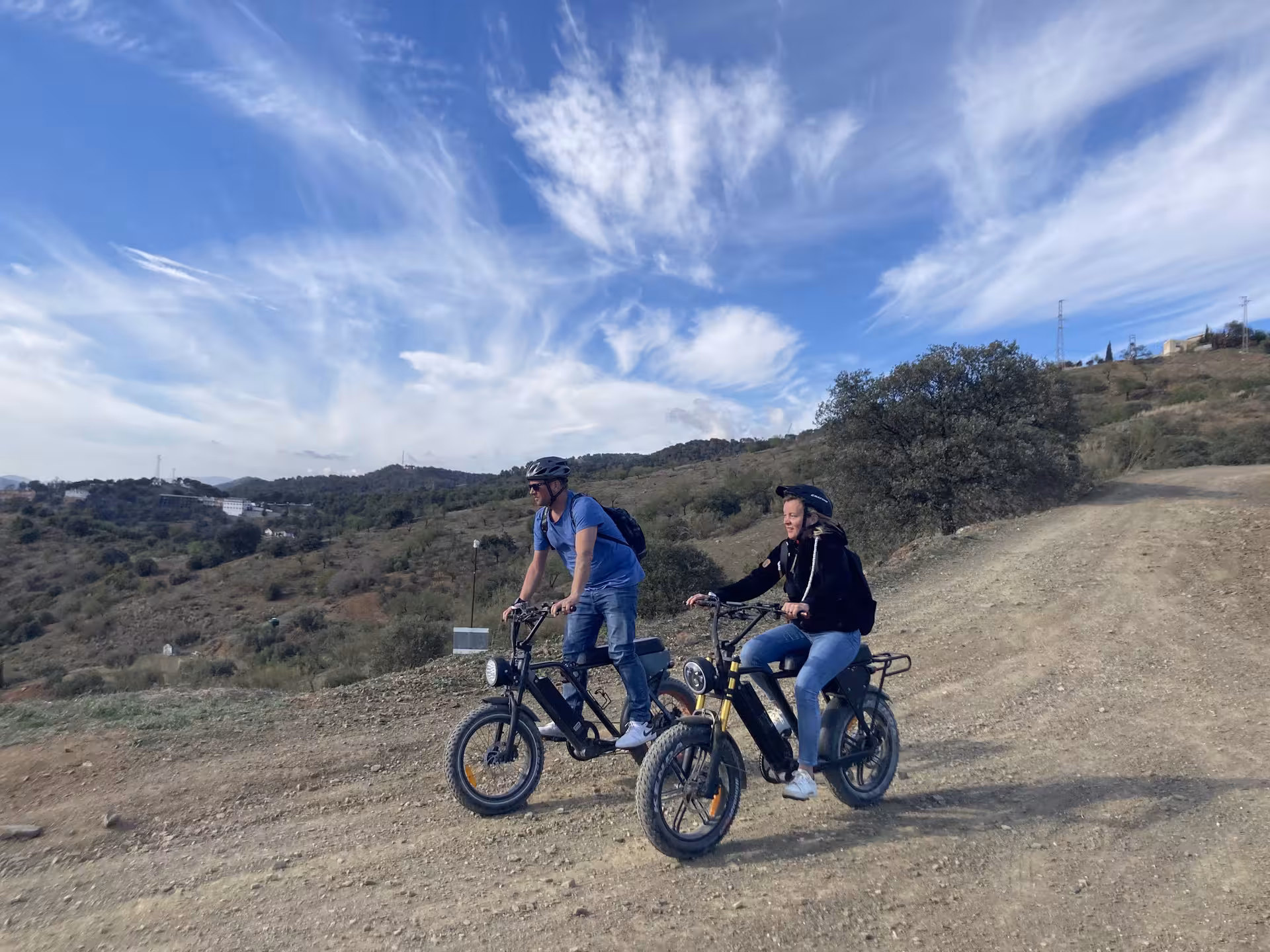 Couple riding electric fat bikes on rugged hillside trail with wide tires, perfect for 4-hour coastal views rental