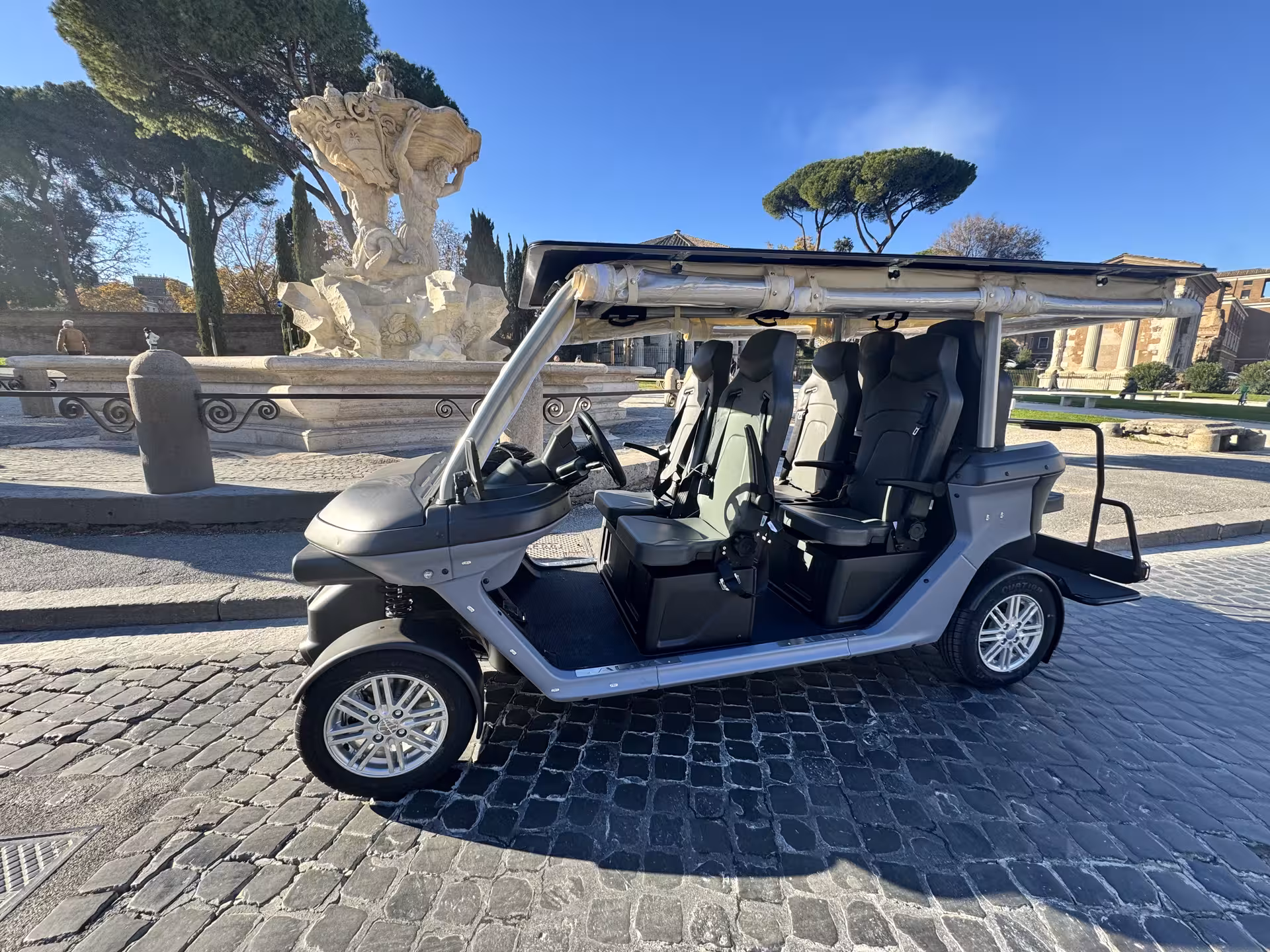 Modern electric golf cart ready for Civitavecchia to Rome VIP tour, parked by ancient fountains and Roman ruins