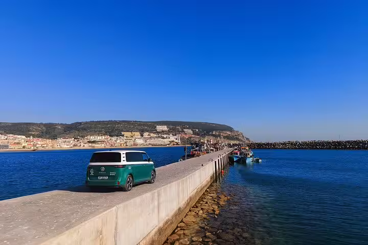 Electric ID Buzz parked on a scenic pier in Sesimbra with coastal views and clear blue skies.