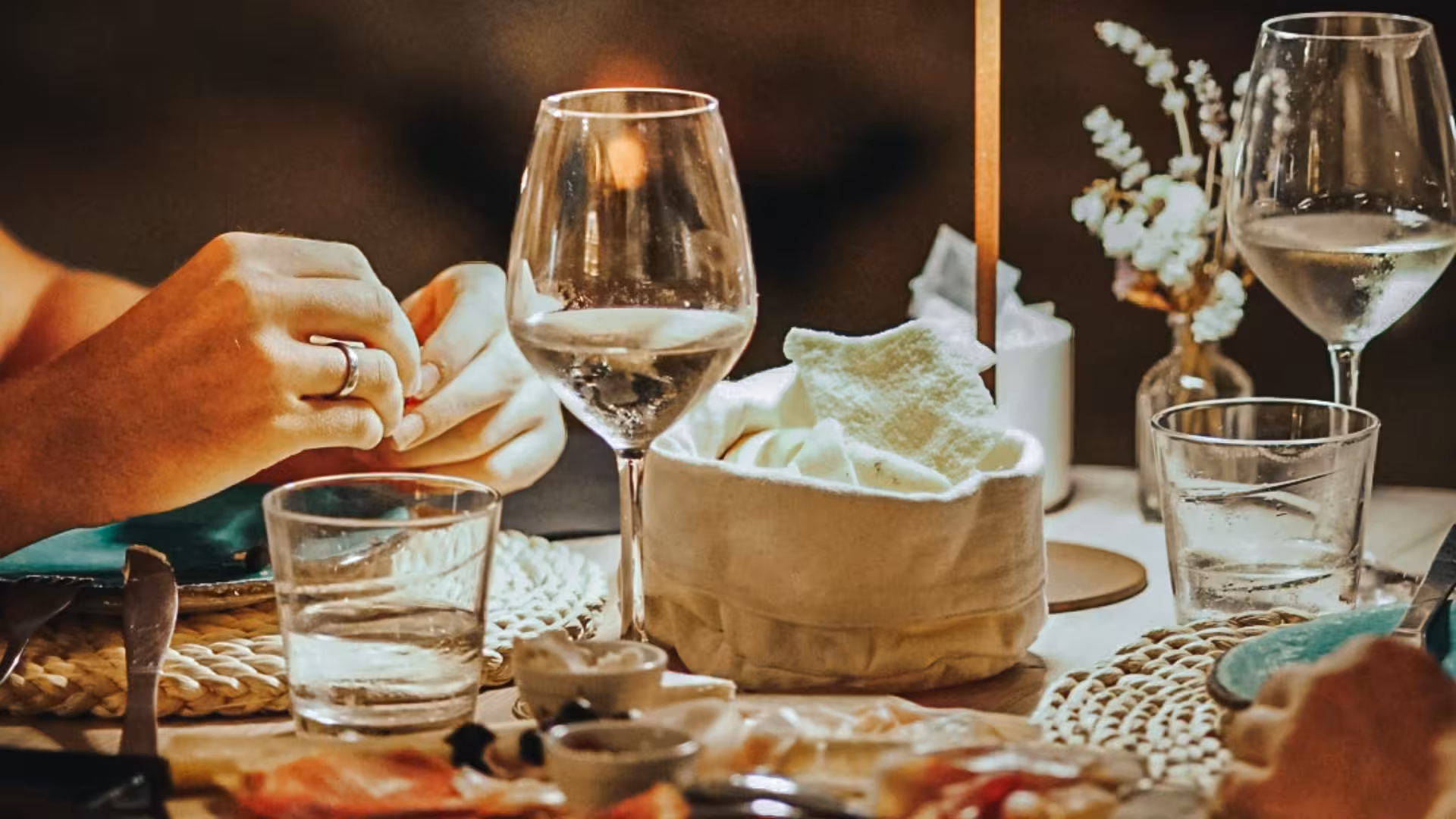 Close-up of an elegant dinner table with wine glasses, bread basket, and diners enjoying a meal in a villa.